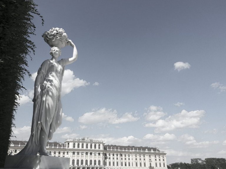 Statuette einer Dame mit Blumen, vor einem historischen Gebäude unter einem Himmel.